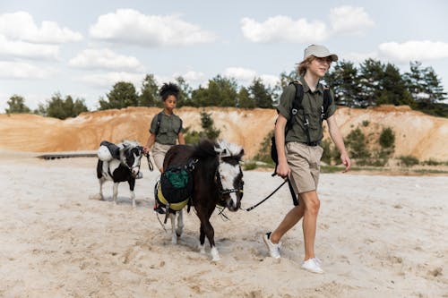 Free Teenage Boy and Girl Walking with Donkeys on Sand Stock Photo