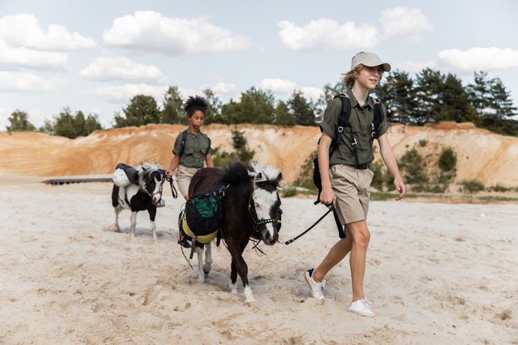 Teenage Boy And Girl Walking With Donkeys On Sand