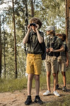 A group of teenagers in khaki shorts and shirts exploring a forest with binoculars, discovering nature.