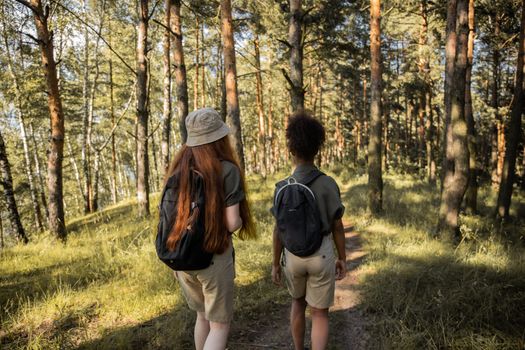 Two girls wearing backpacks enjoy a summer hike through a lush forest trail.