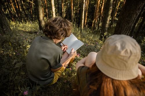 Free Two teenagers sketching in a serene forest environment surrounded by nature's tranquility. Stock Photo