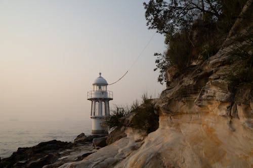 White Lighthouse on Rock Formation Near Body of Water