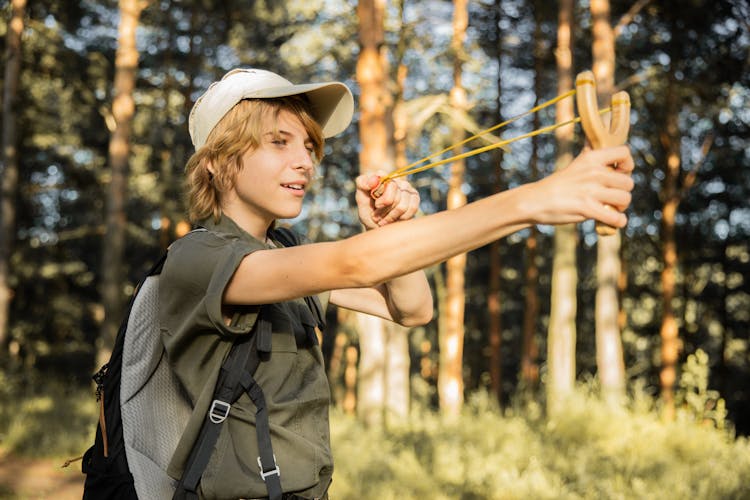 Teenager On An Adventure In A Forest Shooting From A Slingshot