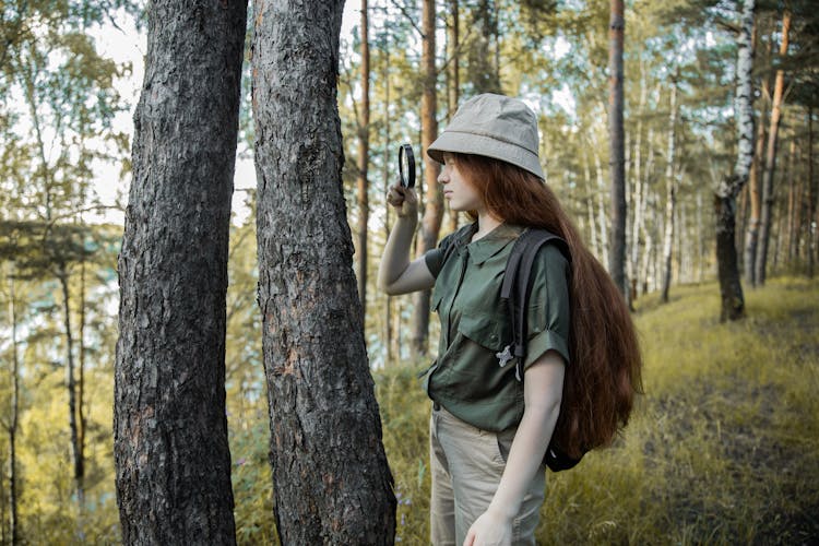 Girl Scout With Magnifying Glass Looking At Tree Trunk