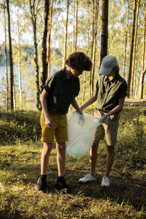 Free Two children participate in a forest cleanup, collecting litter during a summer day. Stock Photo