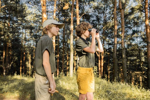 Two teenage boys exploring a lush forest using binoculars on a sunny summer day.