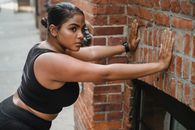 Woman in Black Tank Top Leaning on Brick Wall