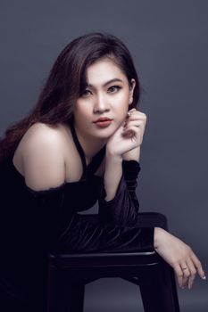 Elegant portrait of a brunette woman in a black dress against a gray backdrop, exuding confidence and grace.