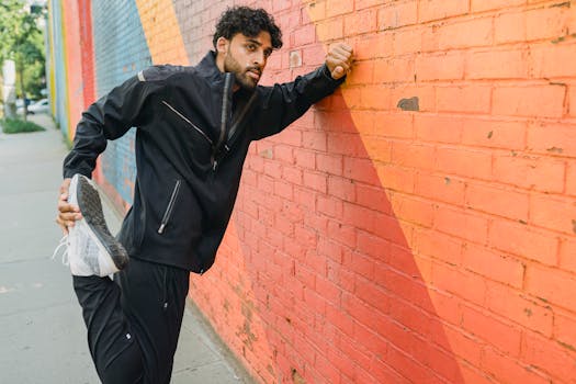 Athletic man in sports attire stretching against a vibrant mural wall outdoors.
