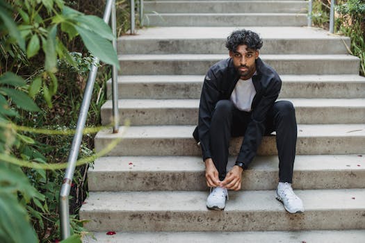 一名穿着运动服的男子坐在户外台阶上系鞋带，展现出都市的休闲风格