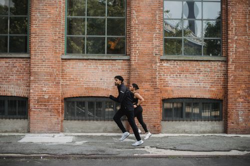 Free A couple jogging together on a city street beside a red brick wall, showcasing a healthy lifestyle. Stock Photo