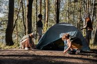 Man in Black T-shirt Sitting on Brown Tree Log Near Gray Tent