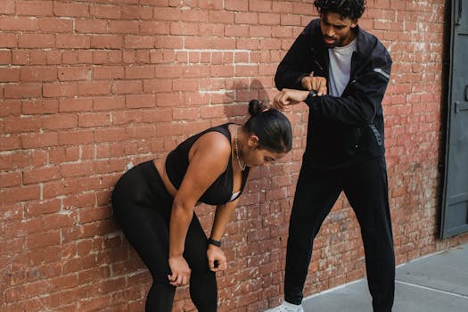 Two people in sportswear pause during outdoor workout against a brick wall.