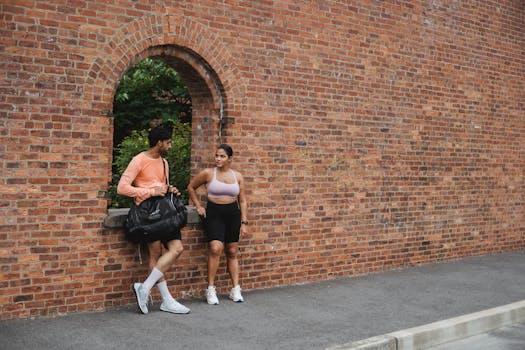 A man and woman in sportswear standing by a brick wall, chatting outdoors.