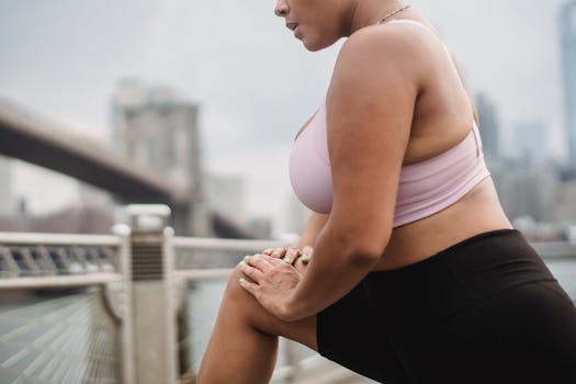 Woman in athletic wear stretching outdoors with Brooklyn Bridge in the background.