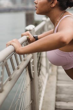 一名身穿粉红色运动服的女人，正侧身于桥栏杆上做俯卧撑，画面突显了健身的毅力与决心