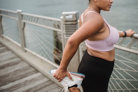 Female athlete in activewear stretching by waterfront, promoting fitness and health.