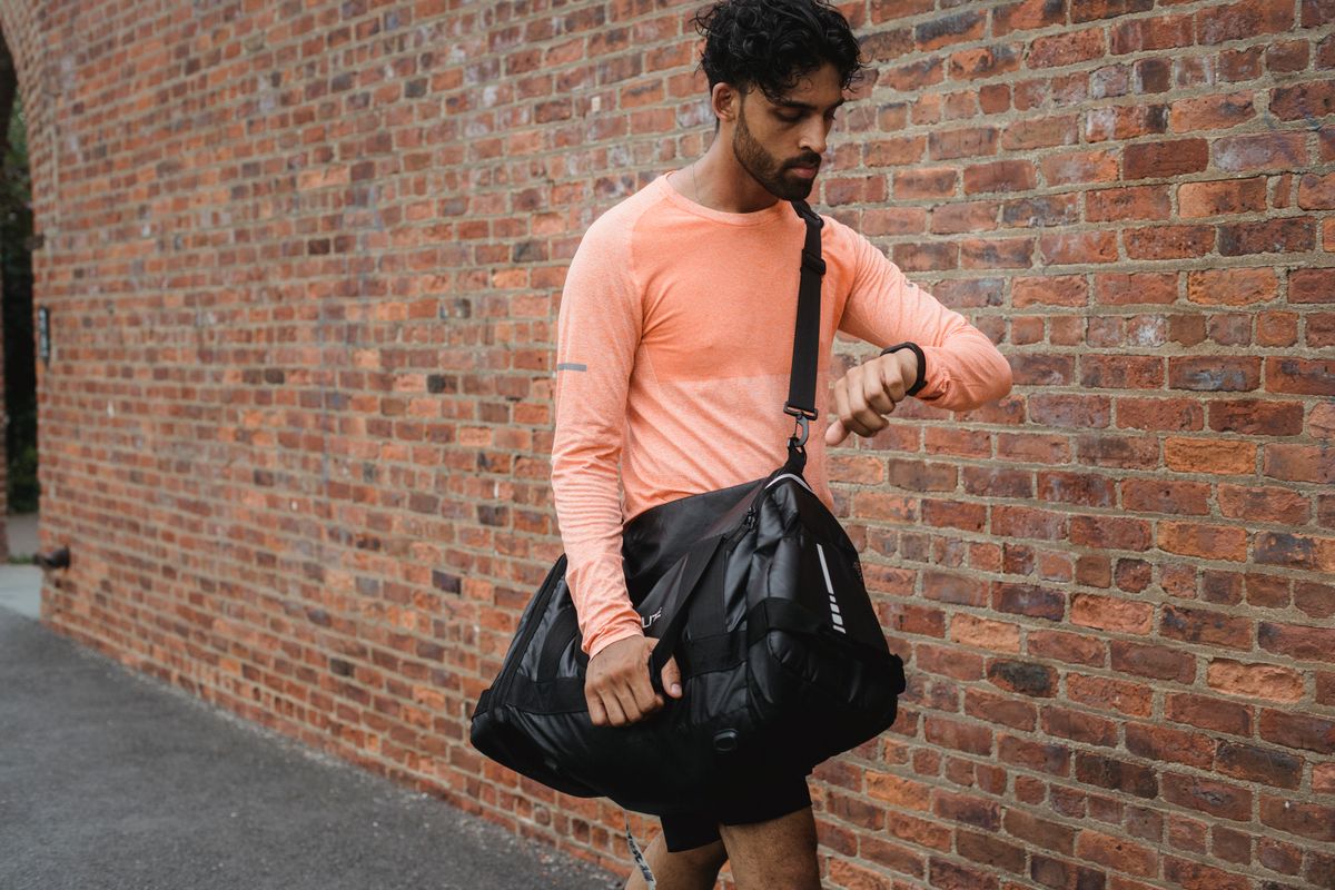 Man carrying a duffle bag while walking near a brick wall