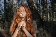 一位红发、雀斑的年轻女子在阳光明媚的森林里拿着白花