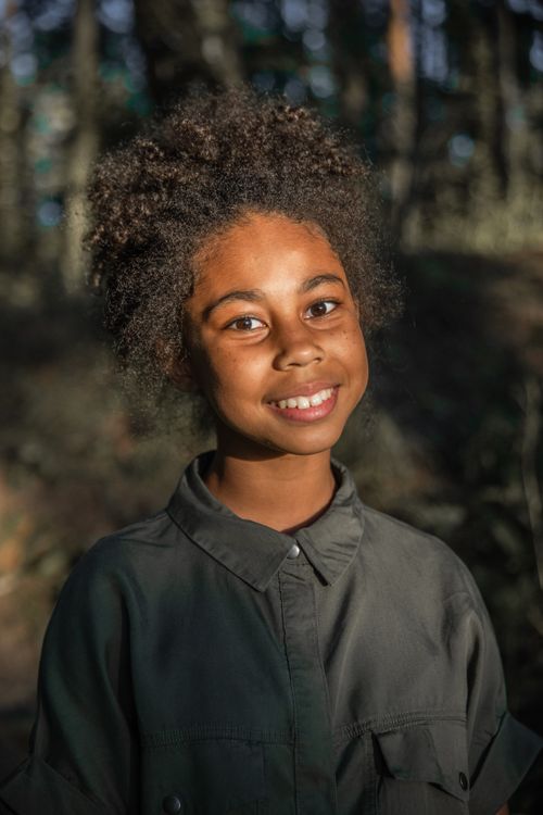 Free Portrait of a cheerful African American girl with afro hair, smiling in a sunlit forest setting. Stock Photo
