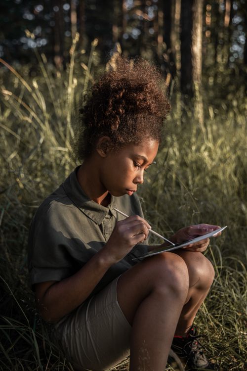 Free A young girl with curly hair enjoys painting outdoors during summer, amidst tall grass. Stock Photo