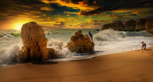 Free Dramatic beach scene with children playing and waves crashing at sunset. Stock Photo