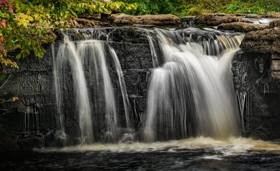 Tranquil waterfall flowing over rocks in a vibrant autumn forest setting.
