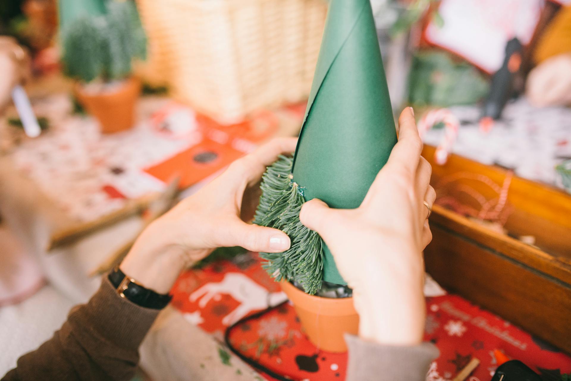 Hands crafting a DIY Christmas tree using green paper and pine leaves for holiday decor.