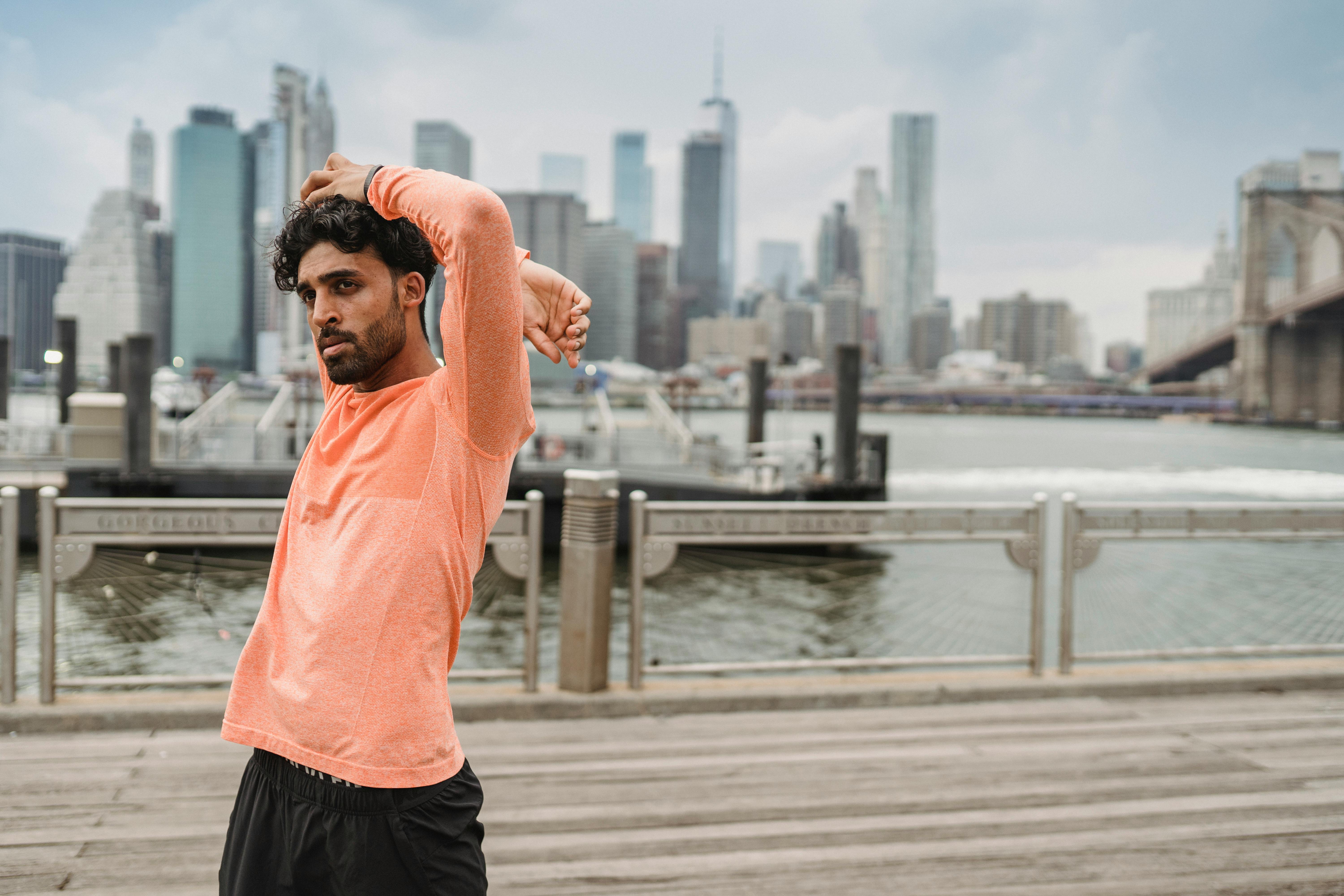 男人在海滨上伸展，背景是布鲁克林大桥和城市天际线