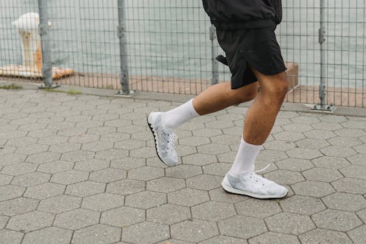 Close-up of a man running outdoors in white sneakers by a waterfront.
