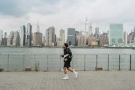 一名男子在城市天际线的背景下，沿着河边的长廊慢跑，展现了城市运动的风貌