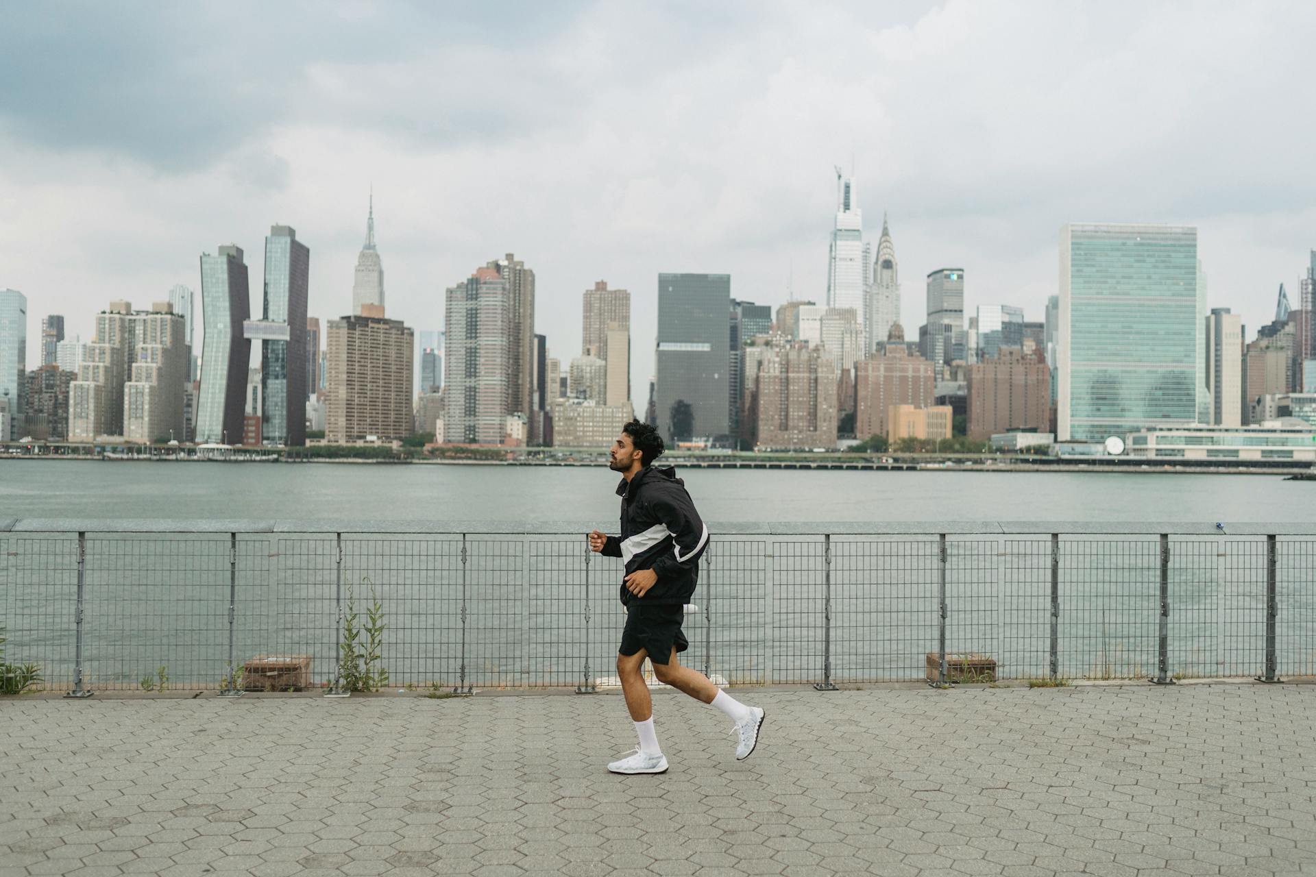 A man jogs along a riverside promenade with a city skyline in the background, showcasing urban exercise.