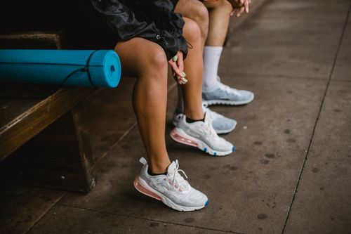 Free Close-up of two people sitting on a bench with a blue yoga mat and stylish sneakers. Stock Photo
