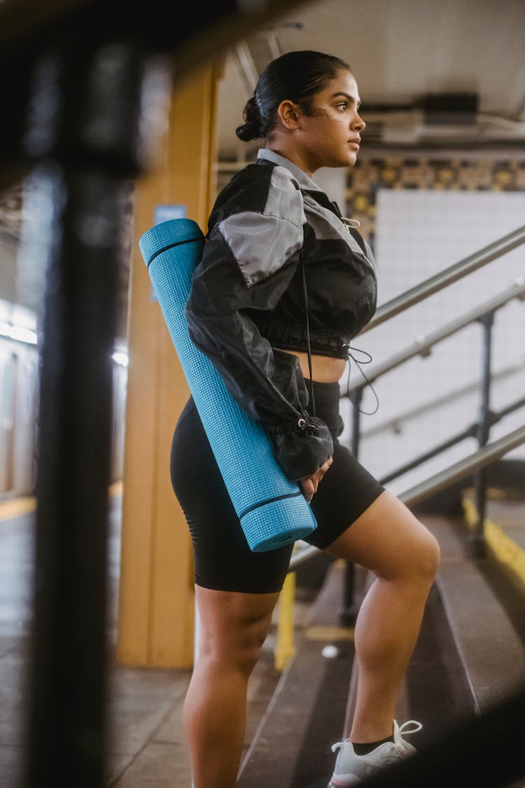 Side View Of A Woman Going Up The Stairs While Carrying Her Yoga Mat