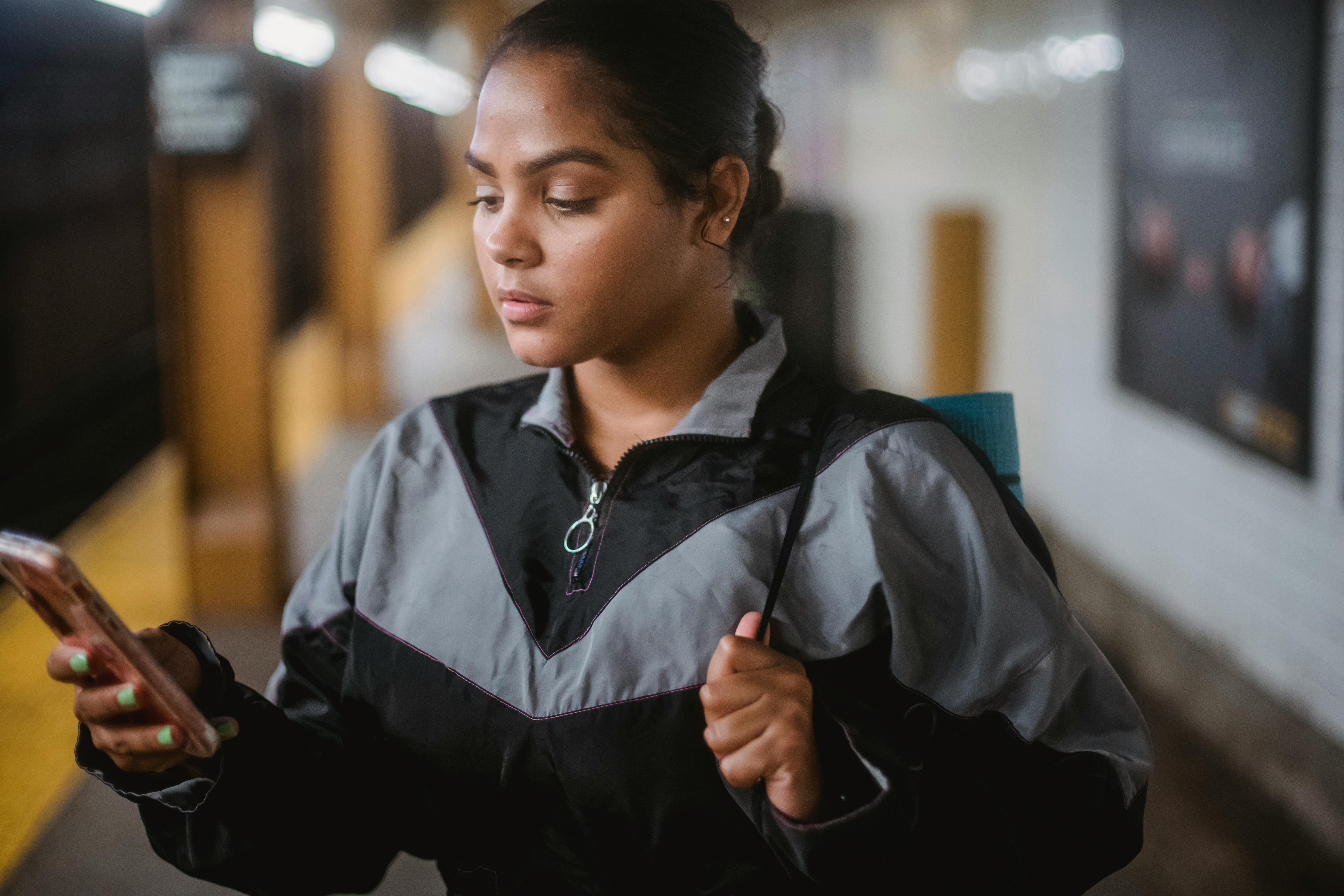 一名年轻女子穿着夹克，在地铁站等车时用着手机