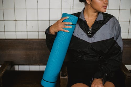 Photo of a Woman in a Black and Gray Jacket Holding a Blue Yoga Mat