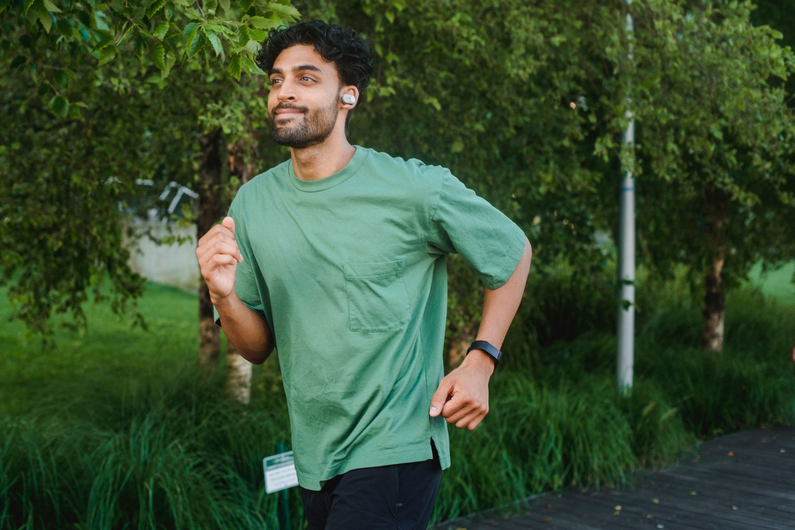 A man running in a park with earbuds and a fitness band