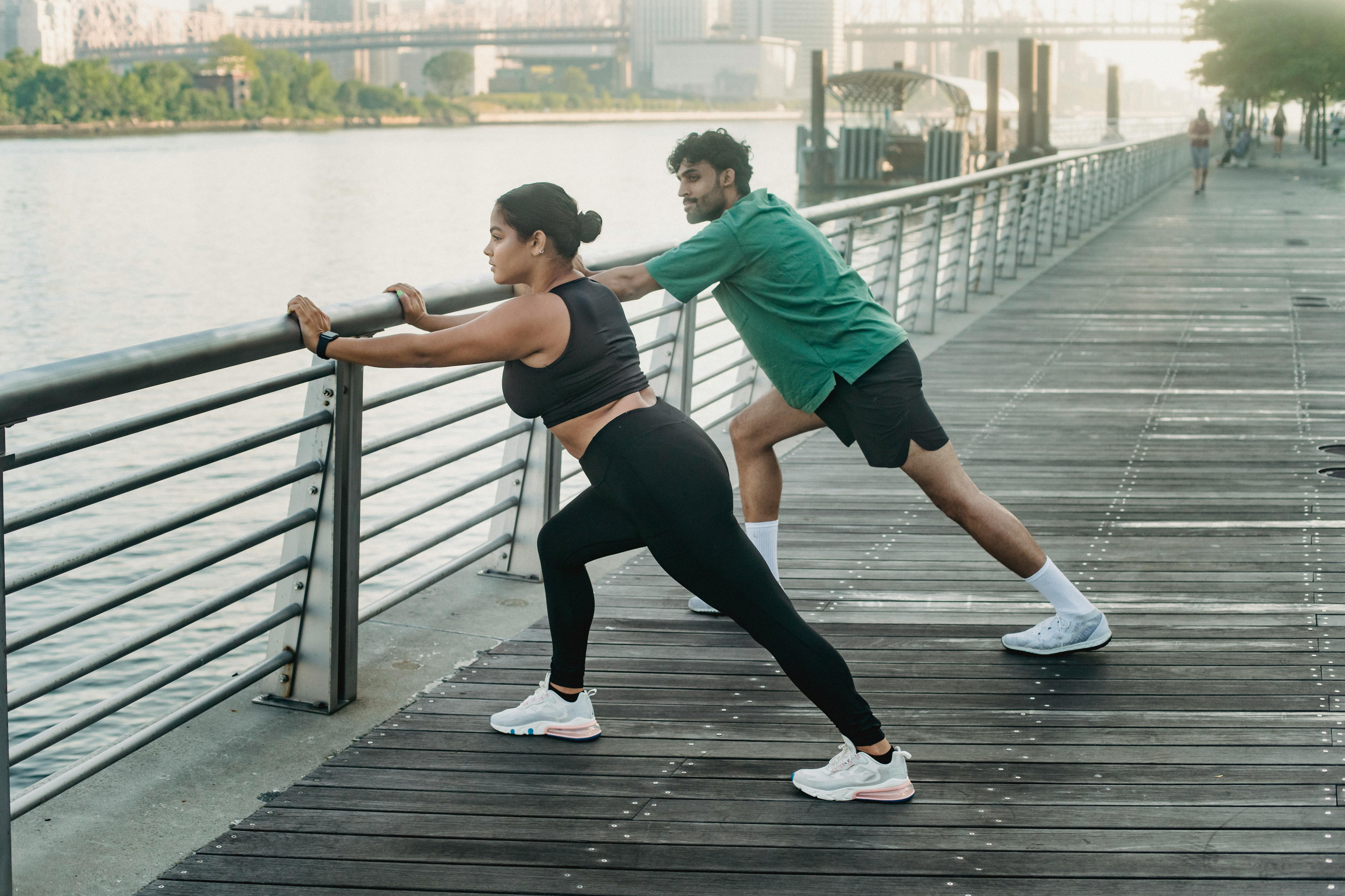 一对男女在河边的木板路上伸展身体，拥抱健康的生活方式