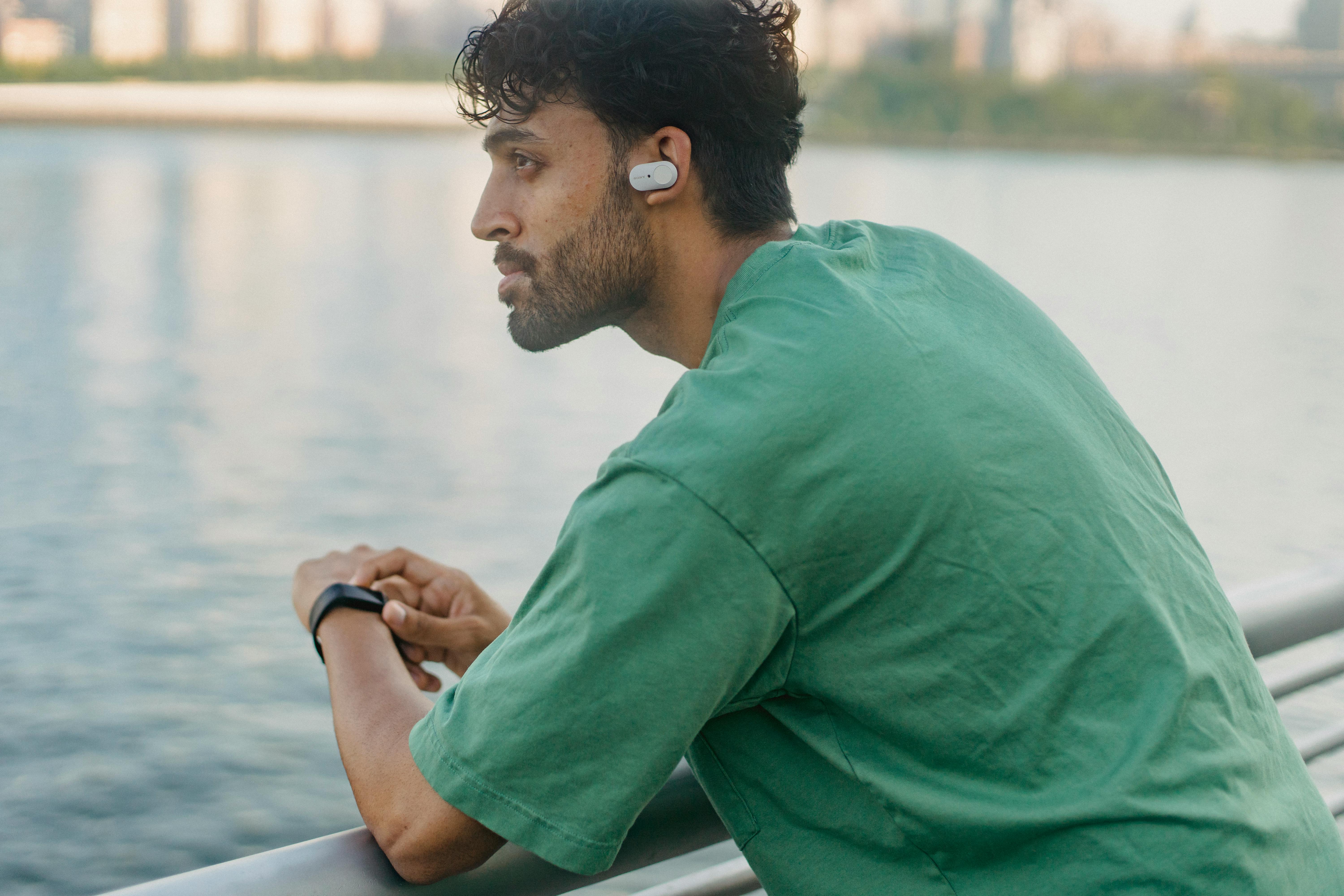 在海滨，一个穿着绿色衬衫、戴着耳机的人靠在栏杆上沉思