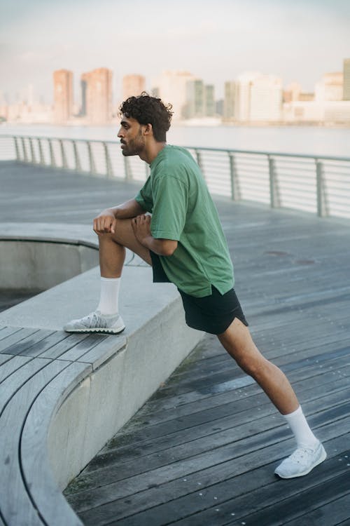 Man in Green T-shirt Stretching His Leg on the Bench