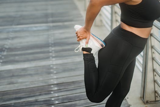 A woman in activewear stretching her leg while standing on a wooden platform outdoors.