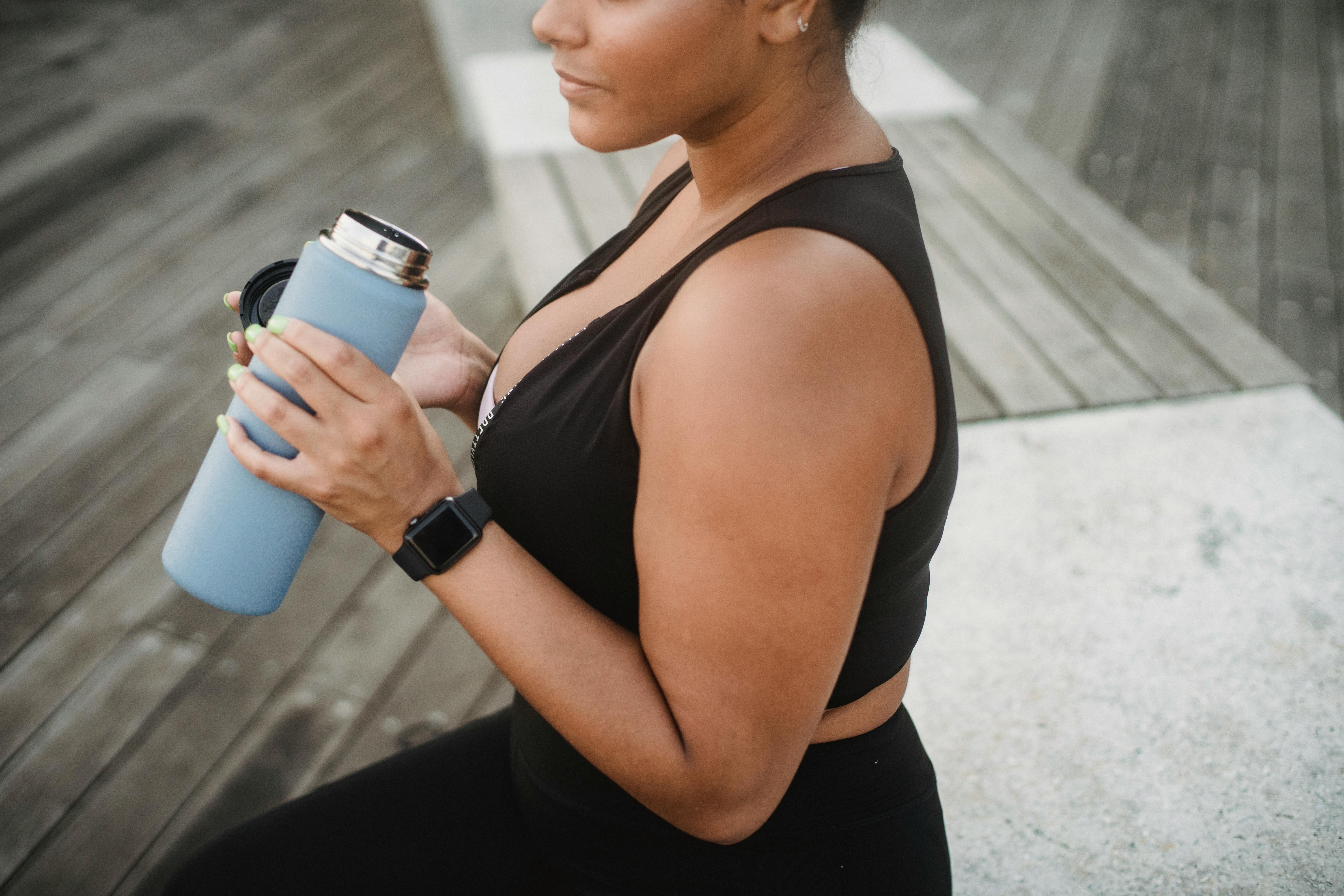 A woman in a sports bra holding a water bottle on a wooden deck. Perfect for health and fitness concepts.