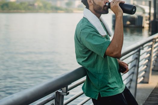 一个男人穿着运动服在河边喝水，拥抱健康的生活方式