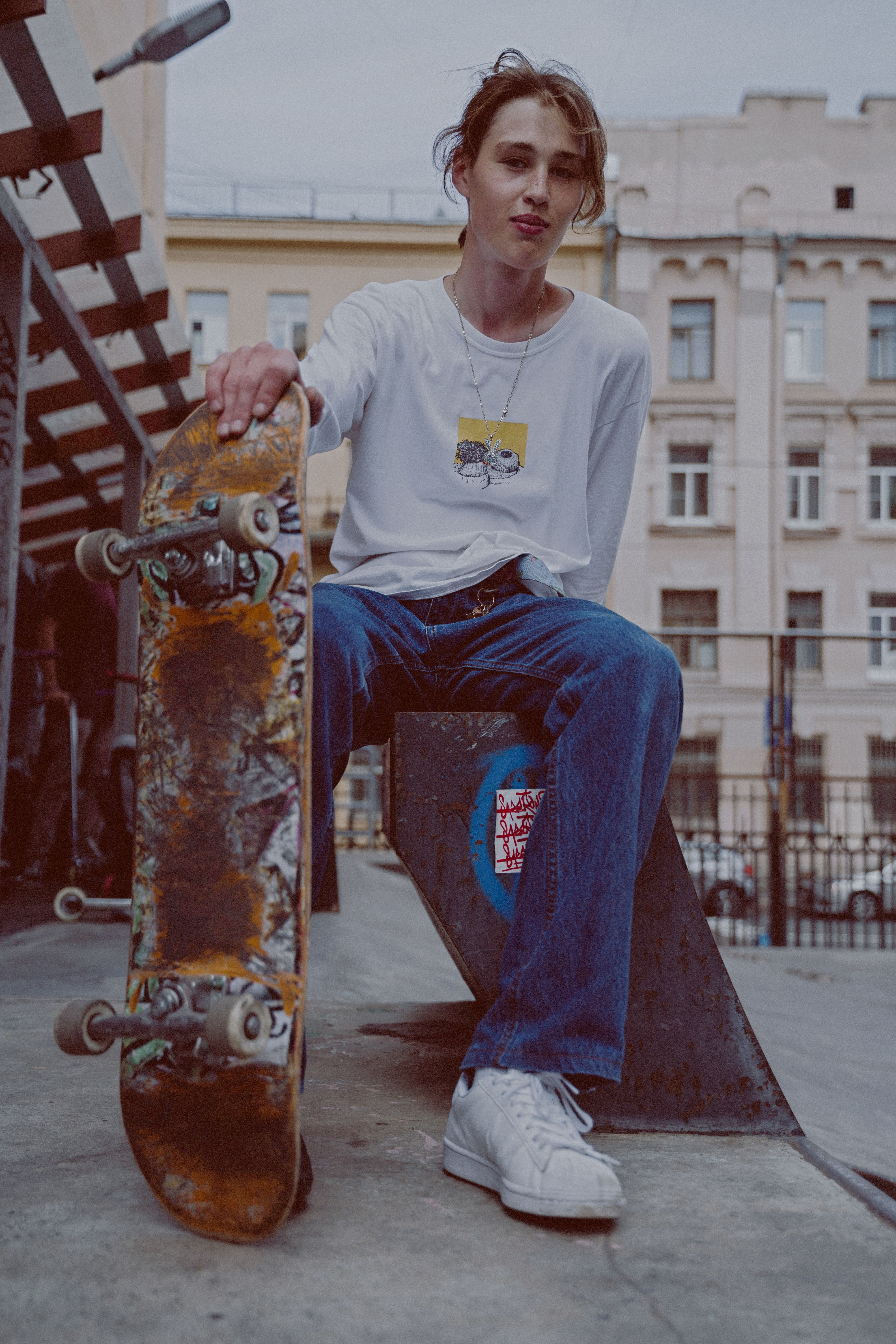 Young skateboarder sitting on concrete bench in urban setting with skateboard. Casual and stylish.