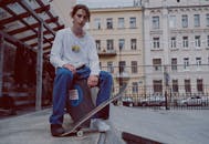Man Stepping on Skateboard While Sitting on Ledge