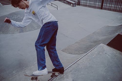 Мужчина в белой рубашке с длинным рукавом и синих джинсовых джинсах катается на скейтборде