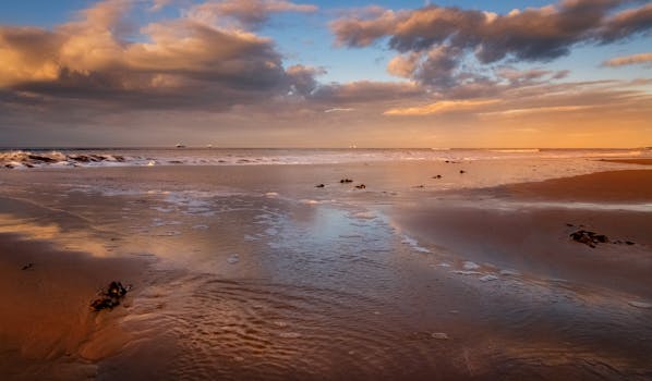 Peaceful seascape at sunset with moody clouds reflecting on wet sand.