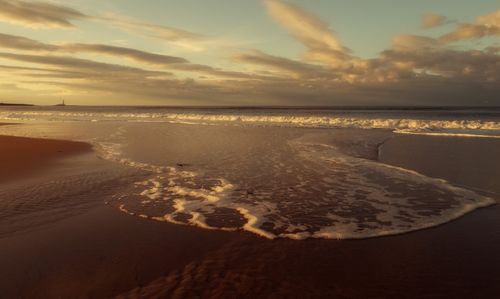 Free A tranquil beach scene captured at sunset with soft waves and a golden sky, perfect for a relaxing wallpaper. Stock Photo