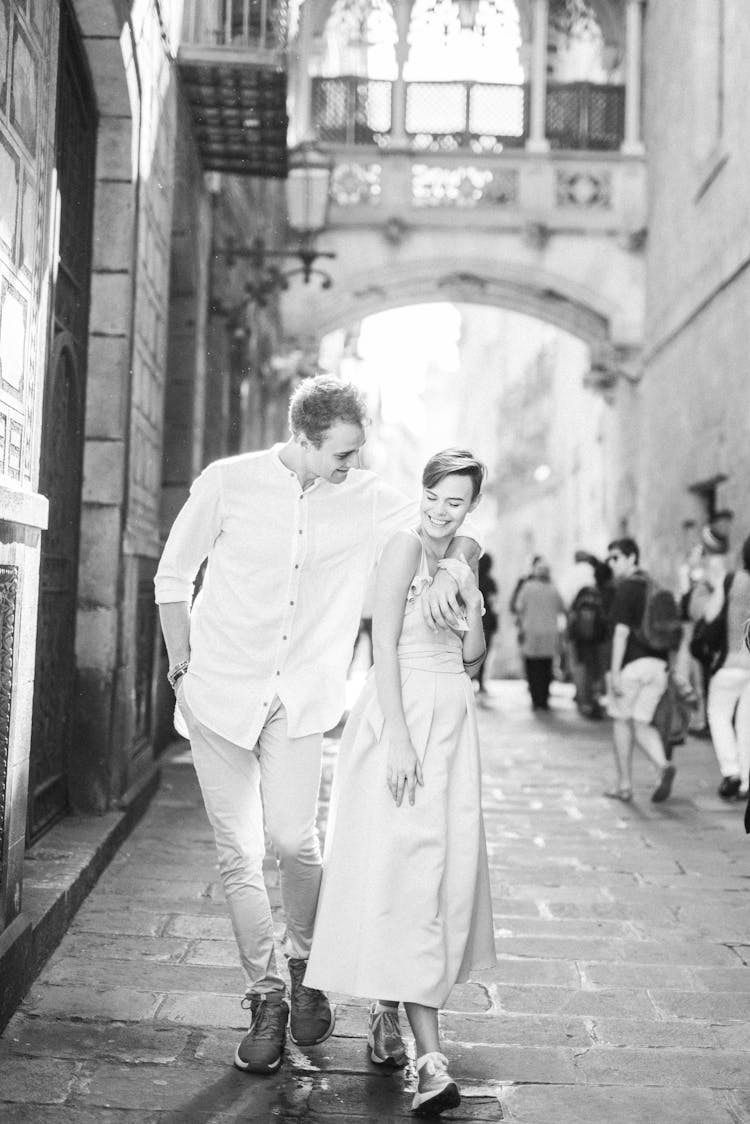 A Grayscale Photo Of A Couple Standing On The Street Together