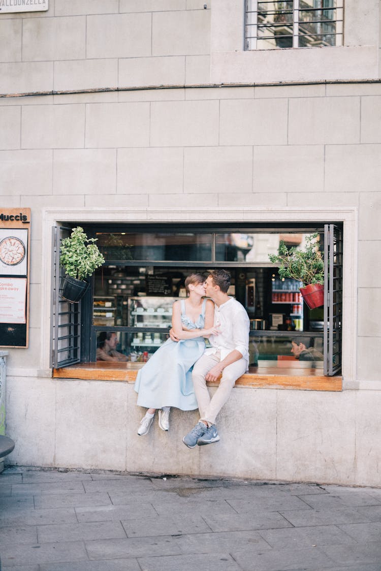 Man And Woman Sitting On A Store Window And Kissing